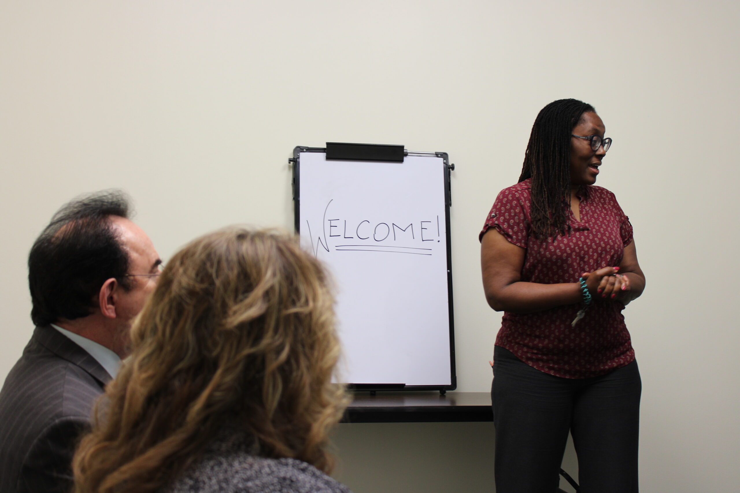 woman standing at whiteboard with welcome written on board with people looking on
