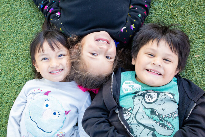 3 kids smiling for camera while laying in grass