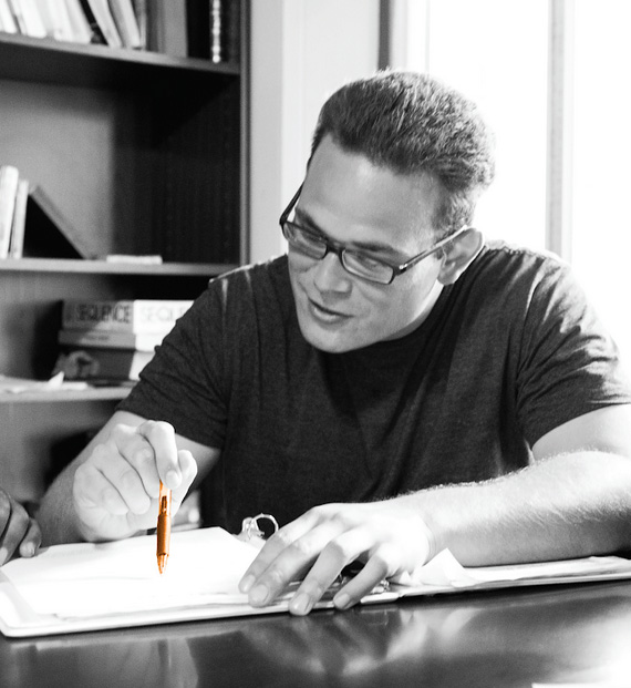 man wearing glasses writing in a notebook at the table